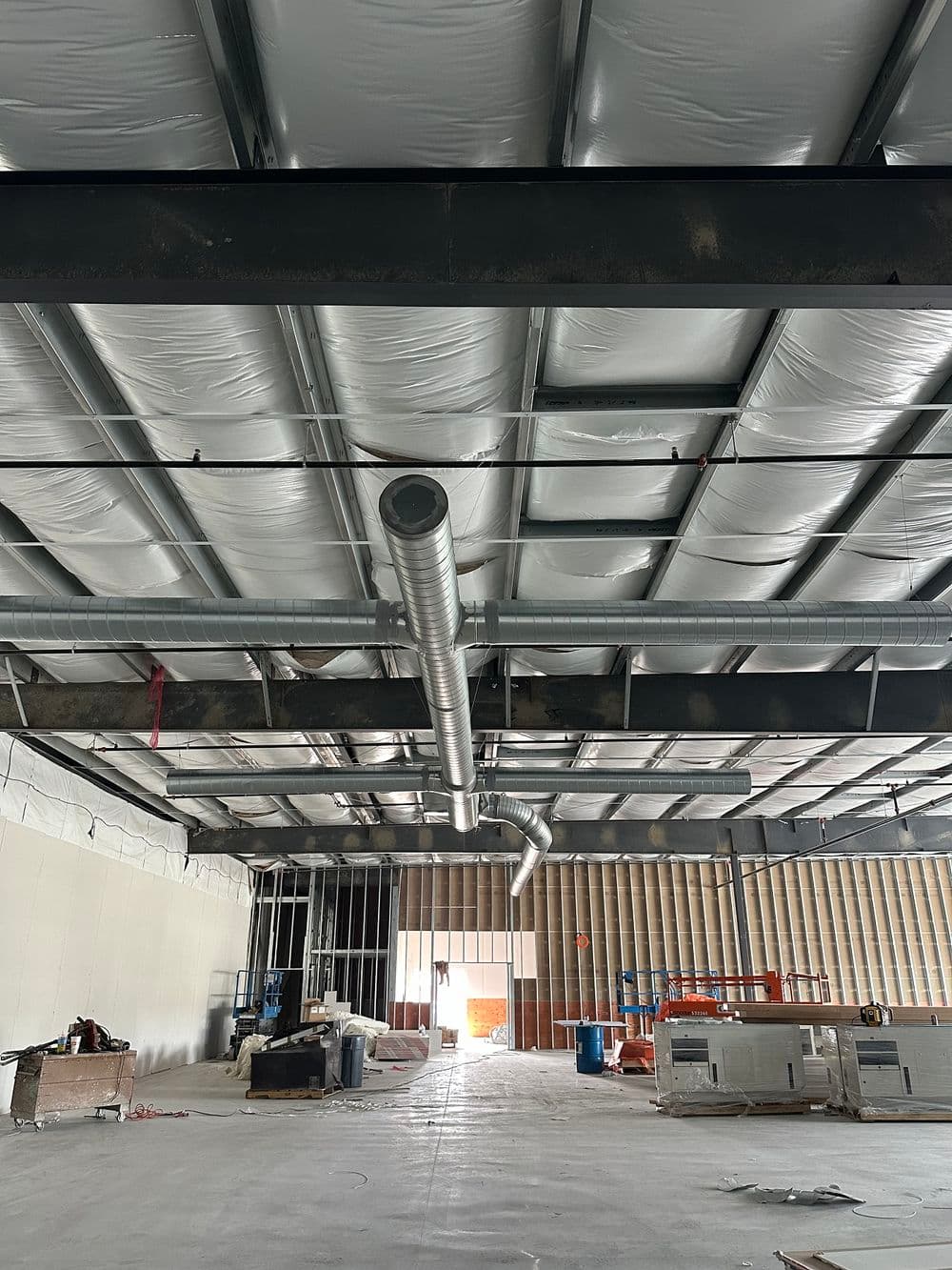 Interior construction site showing exposed ceiling, HVAC ductwork, and unfinished walls.