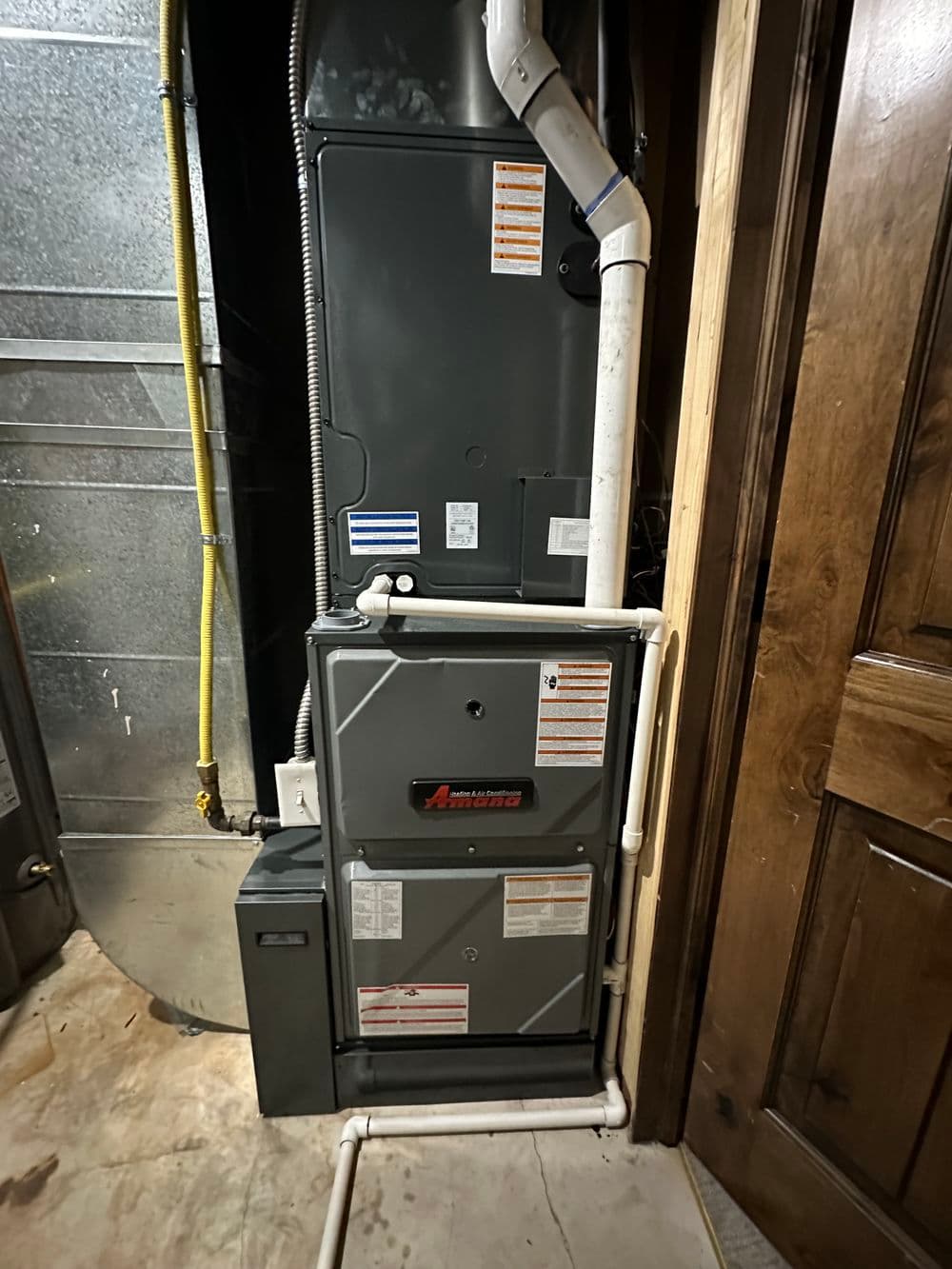 Vertical arrangement of a heating system with labeled pipes and a wooden door in the background.