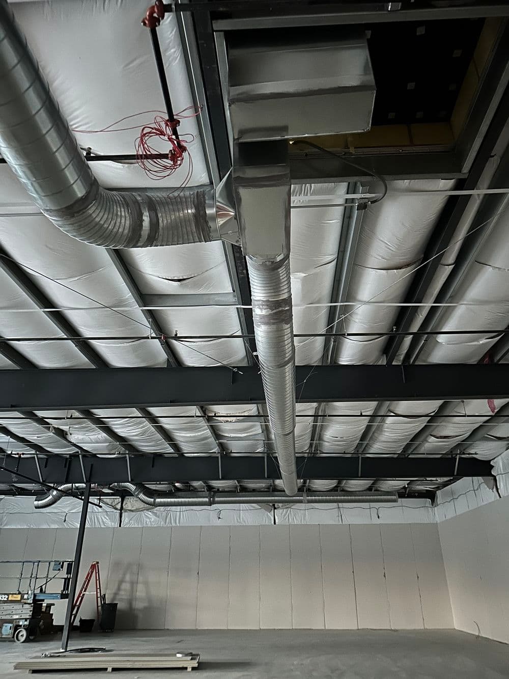 Modern industrial ceiling with exposed ductwork and metal beams in an empty warehouse space.