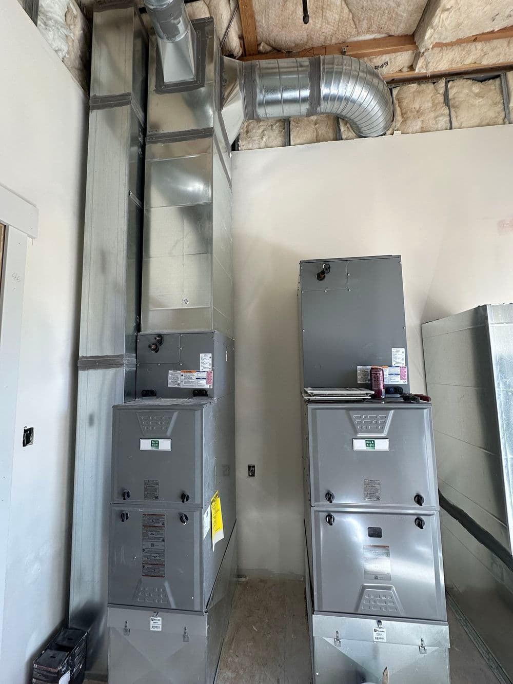 HVAC system installation featuring two gray furnaces and ductwork on a bare wall.