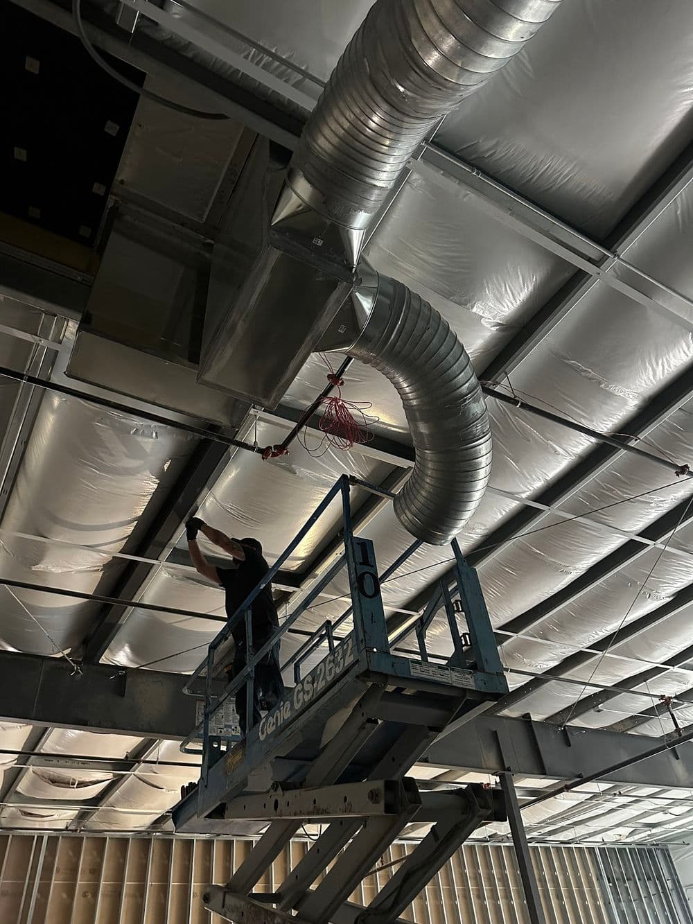 Technician working on HVAC duct installation from lift in ceiling of commercial building.