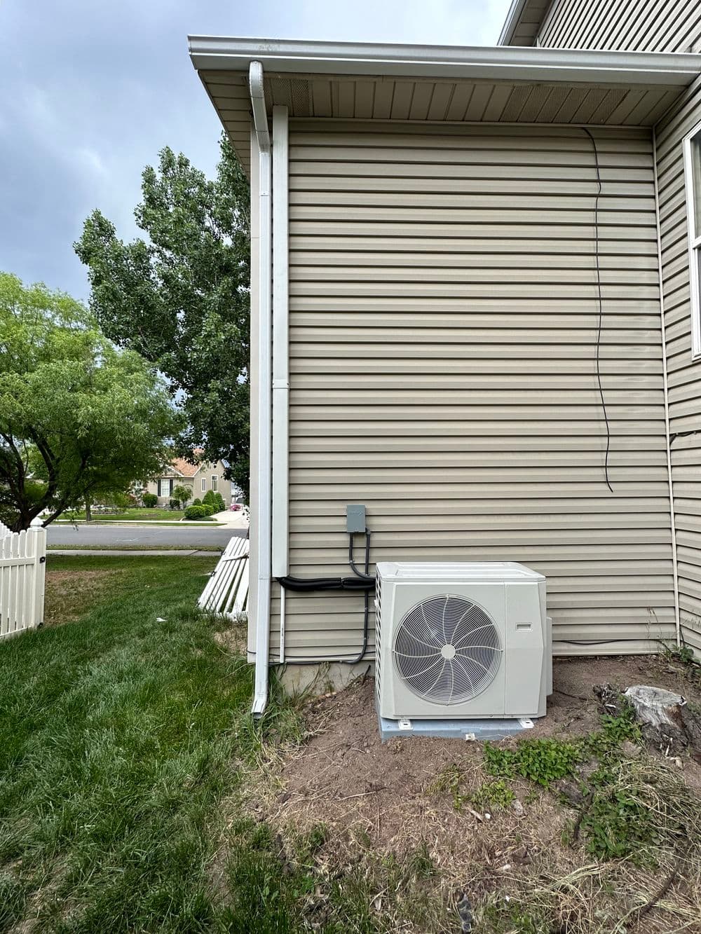 Air conditioning unit installed beside a house, with green grass and trees in the background.