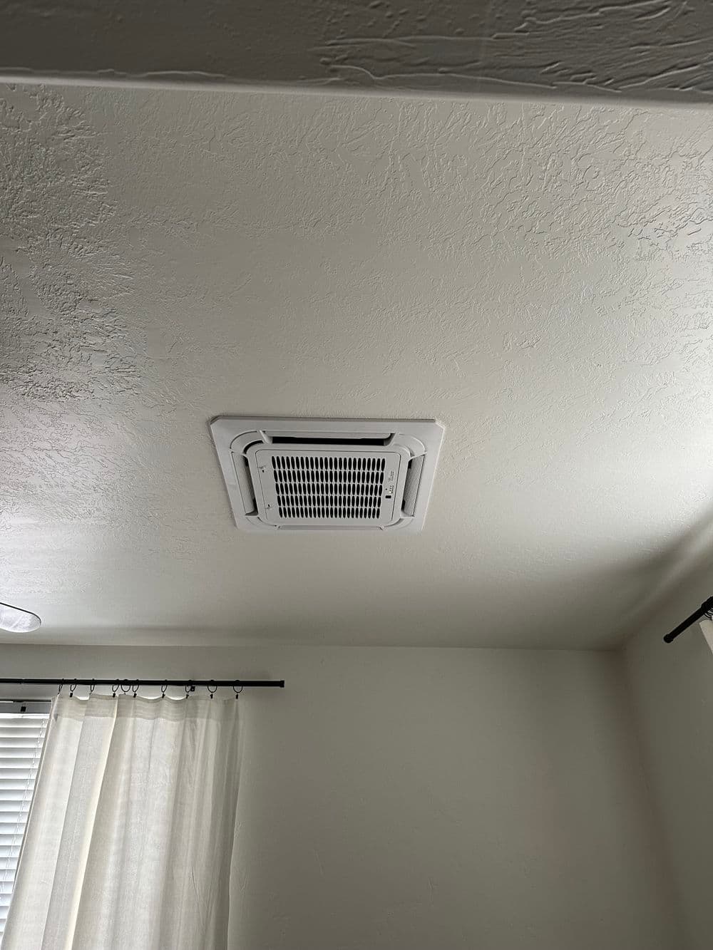 Ceiling air conditioning unit installed in a room with natural light and white curtains.