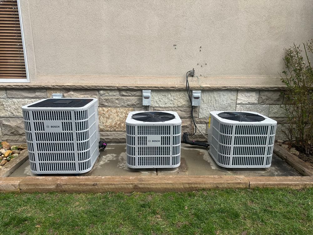 Row of three air conditioning units installed beside a building, surrounded by grass.