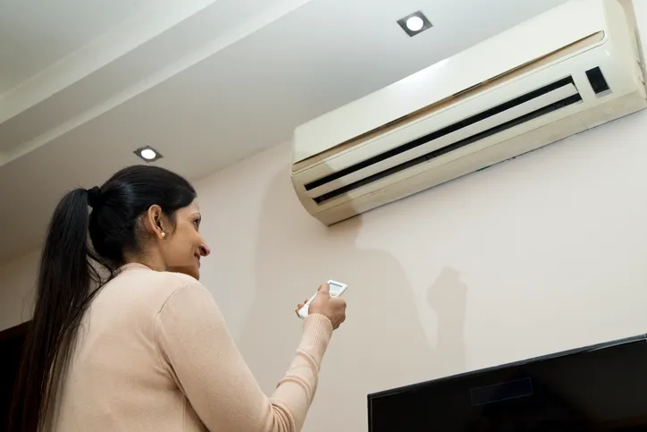 Mini Split Air Conditioner In West Jordan, UT 1 A woman smiling and holding a remote control pointed at a wall-mounted mini-split air conditioner.