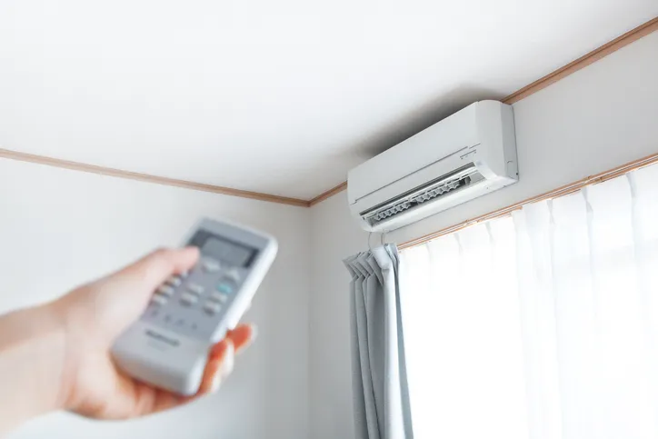 Mini Split Ac Installation In West Jordan, UT 1 A person's hand holding a remote control pointed at a wall-mounted mini-split air conditioner.