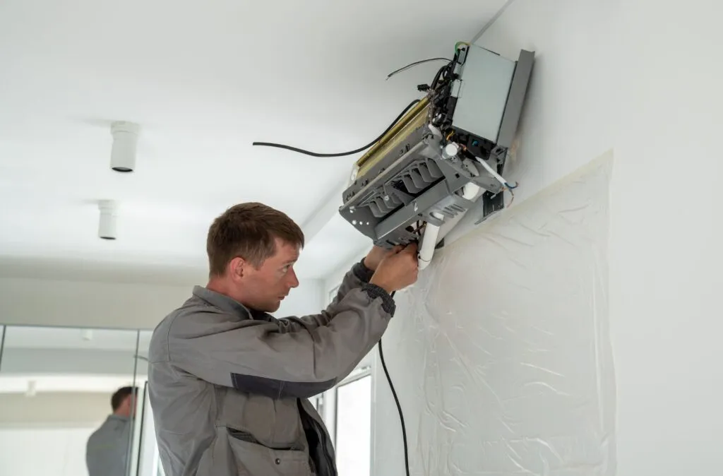 HVAC Services in Sandy, UT 1 Technician in gray jacket using tools to install or repair wall-mounted air conditioning unit